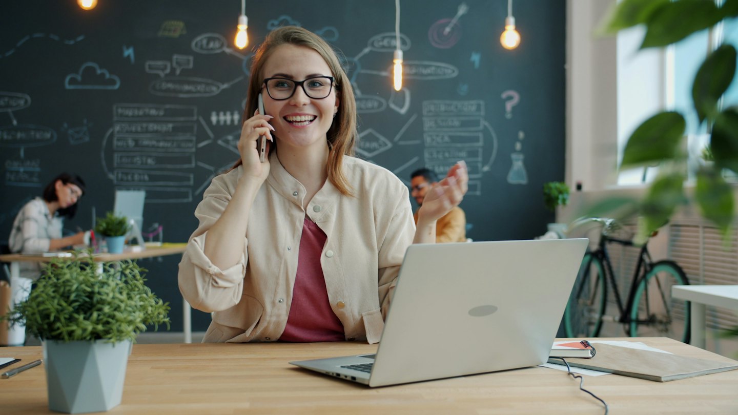 Eine Frau mit Brille telefoniert in einem modernen Büro.